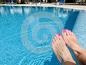 Woman's feet with red nail polish on the toes. Relaxing near swimming pool.