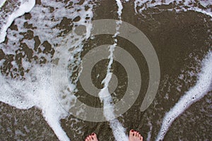 A woman`s feet with red toenails in the foamy, shallow water of the Pacific Ocean on a sandy beach in Hawaii