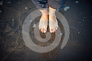 Woman`s feet on sandy beach, standing in ocean water, copy space. Pedicured feet with red nail polish on toes in the sea. Bare