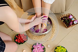 woman`s foot washing procedure before spa treatment in a salon done by a masseuse; a silver bowl with water, rose petals and flow
