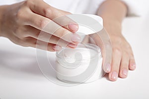 Woman`s gentle hands with perfect manicure and a jar of cream