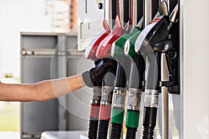 A woman`s gloved hand reaches for a gasoline pump pistol at a gas station. Refueling the car