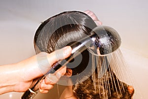 Woman`s hair is washed in the shower with shampoo with water, close-up white background, toned