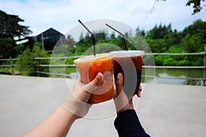 Woman& x27;s hand. 2 girl friends raising a glass of iced coffee and iced tea. Natural background.