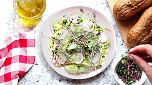 Woman's hand adding microgreens to fresh homemade salad. Healthy food and dieting concept