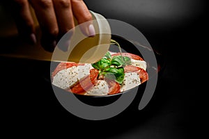 Woman& x27;s hand adds sauce in a bowl with tomatoes and soft cheese with greens photo