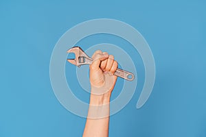 Woman& x27;s hand with an adjustable wrench against blue background