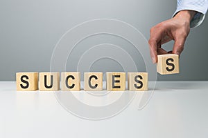 Woman`s hand adjusting `success` word made of wooden blocks. Success word from wooden blocks on desk. Business success