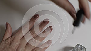 A woman`s hand applies a nail polish fixative to her nails. White background. Close-up on the fingers