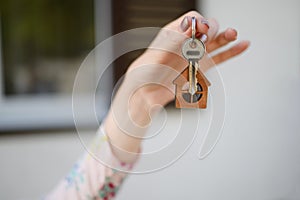 Woman& x27;s hand on the background of the house with the keys to the new house, focus on the keys. Real estate concept