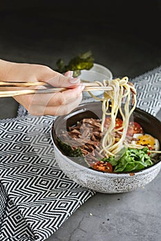 a woman`s hand with a beautiful manicure holds wooden sticks with noodles. there is a napkin on the gray table and a plate