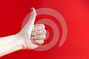 Woman`s hand with beige manicure  on red background thumb raised up, like concept