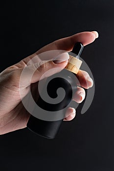 Woman& x27;s hand with a black frosted glass bottle of beauty oil on a black background. Cosmetic products concept. Copy