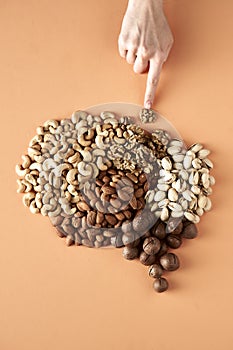 Woman`s hand and brain made up of nuts isolated on beige background, healthy snack, concept photo for food blog or ad