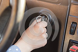 Woman`s hand on car`s key, tries to start engine, turn on key in keyhole, auto`s panel and wheel in background. Key inserted in lo