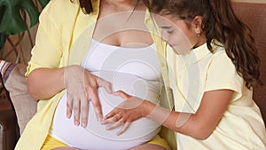 A woman`s hand and a child`s hand make a heart on a pregnant woman`s stomach. Family values. Waiting for birth. The