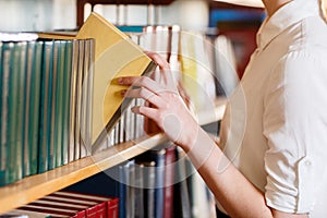 A woman`s hand chooses a book in the library.