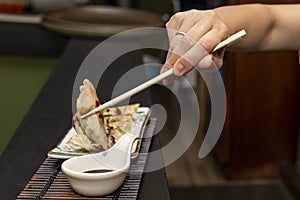 Woman\'s hand with chopsticks dipping a gyoza in soy sauce and then gobbling it up with delight