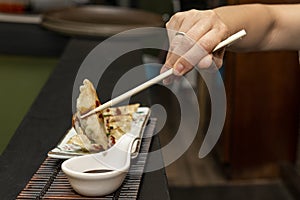 Woman's hand with chopsticks dipping a gyoza in soy sauce and then gobbling it up with delight