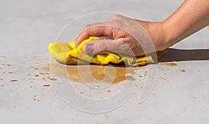 Woman`s hand cleaning spilled water on a cement floor with a yellow floor cloth dishcloth