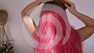 woman\'s hand combing her curled pink hair with a wooden comb. Combing curly hair.