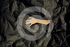 Woman`s hand comes out of hole in black crumpled paper background, a concept photography for beauty blog