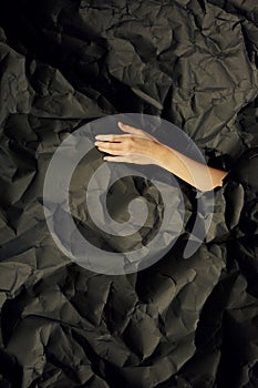 Woman`s hand comes out of hole in black crumpled paper background, a concept photography for beauty blog