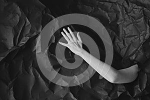 Woman`s hand comes out of hole in black crumpled paper, black and white concept photography for beauty blog or poster