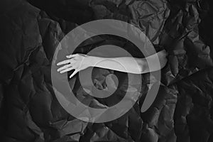 Woman`s hand comes out of hole in black crumpled paper, black and white concept photography for beauty blog or poster