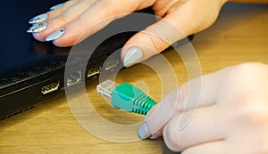 A woman`s hand connects an RJ45 network connector to a laptop