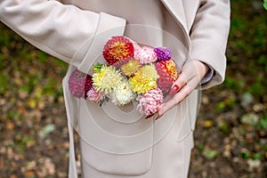 A woman's hand corrects a composition of autumn flowers in the pocket of a beige coat
