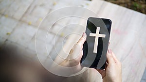 Woman`s hand with cross in screen mobile phone. Concept of hope, faith, christianity, religion, church online