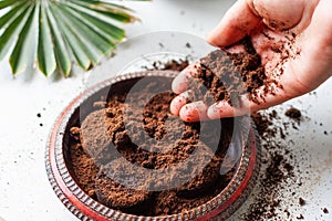 Woman`s hand crumbles coffee grounds into wooden bowl. Coffee grounds used as a body scrub or fertilizer for plants