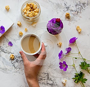 Woman`s hand with cup of coffee, popcorn, wild flowers and viole photo