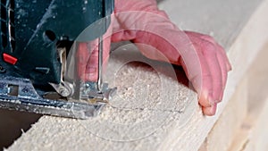 Woman`s hand cuts a board with an electric jigsaw in close-up. Carpentry on wood with a tool, sawdust flies, the saw cuts in a str