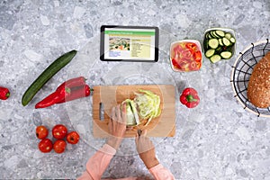 Woman`s Hand Cutting Cabbage With Digital Tablet On Counter