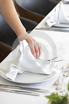 Woman's hand delicately folding a white cotton napkin, decorative technique adding an elegant touch to the table setup