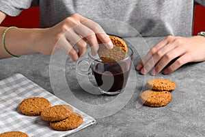 Woman& x27;s hand dipping a cookie into a cup with brew black coffee
