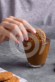 Woman& x27;s hand dipping a cookie into a transparent cup with coffee with milk in the kitchen