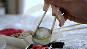 A woman's hand dips futomaki with cucumber in soy sauce.
