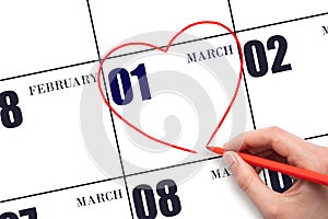 A woman's hand drawing a red heart shape on the calendar date of 1 March. Heart as a symbol of love.