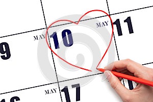 A woman's hand drawing a red heart shape on the calendar date of 10 May. Heart as a symbol of love.