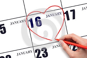 A woman's hand drawing a red heart shape on the calendar date of 16 January. Heart as a symbol of love.