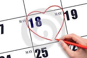 A woman's hand drawing a red heart shape on the calendar date of 18 May. Heart as a symbol of love.