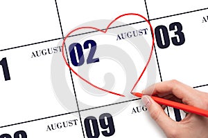 A woman's hand drawing a red heart shape on the calendar date of 2 August. Heart as a symbol of love.