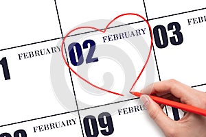A woman's hand drawing a red heart shape on the calendar date of 2 February. Heart as a symbol of love.