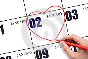 A woman's hand drawing a red heart shape on the calendar date of 2 January. Heart as a symbol of love.