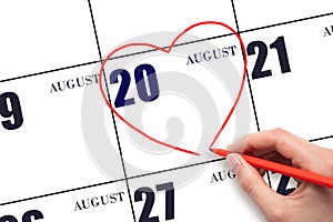 A woman's hand drawing a red heart shape on the calendar date of 20 August. Heart as a symbol of love.