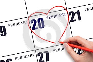 A woman's hand drawing a red heart shape on the calendar date of 20 February. Heart as a symbol of love.