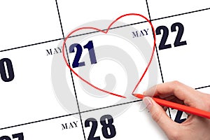 A woman's hand drawing a red heart shape on the calendar date of 21 May. Heart as a symbol of love.